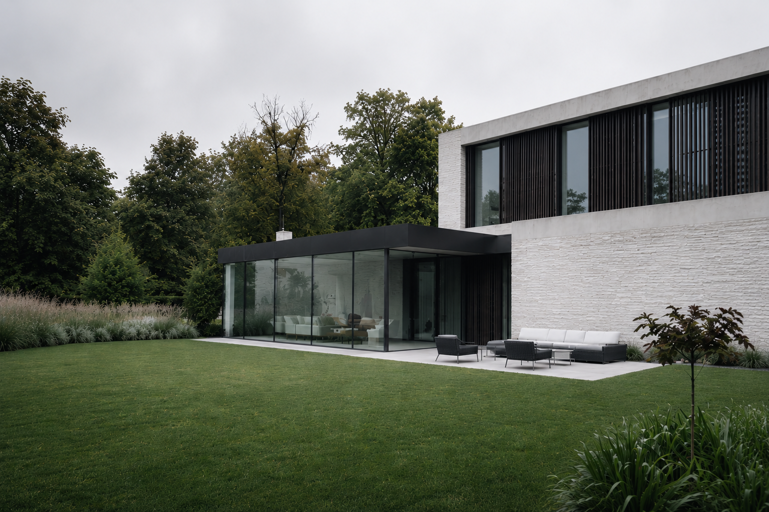 Garden view of a white brick villa with a glazed single-storey pavilion opening onto a paved terrace, lawn and ornamental grasses under an overcast sky